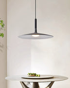 Clérachic grey pendant light above a round stone table with a bowl of limes, in front of a pale curved wall.