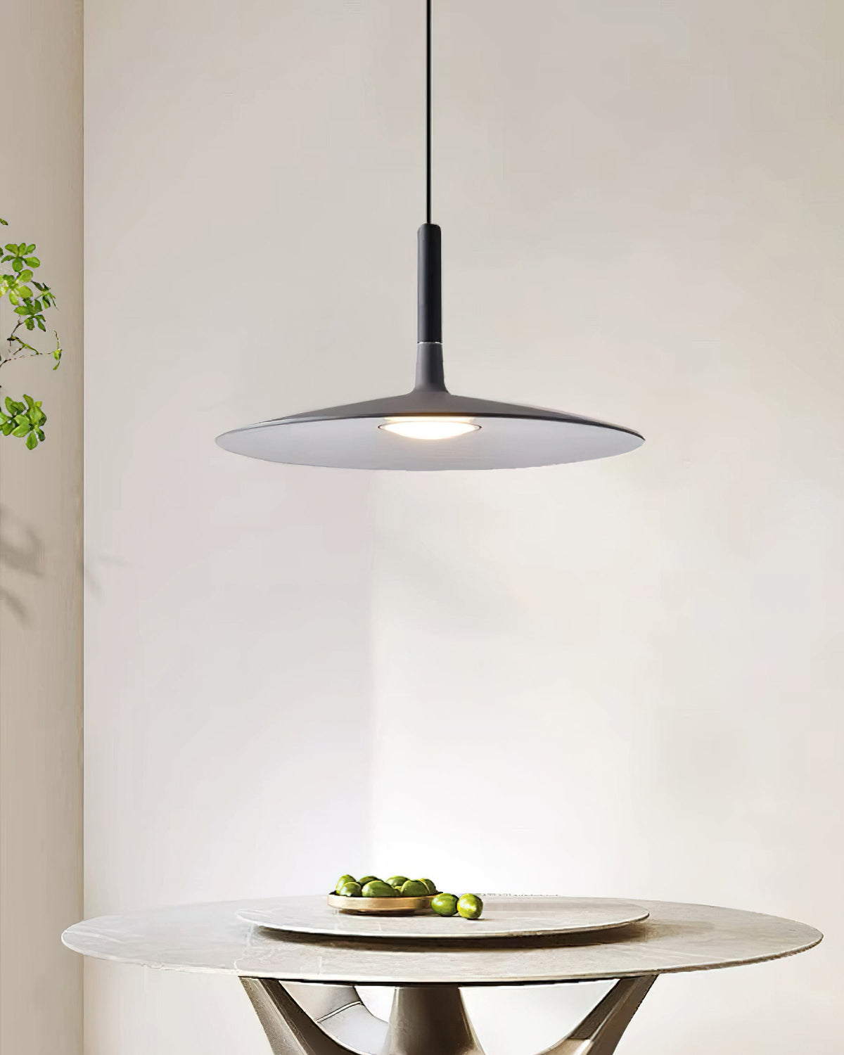 Clérachic grey pendant light above a round stone table with a bowl of limes, in front of a pale curved wall.