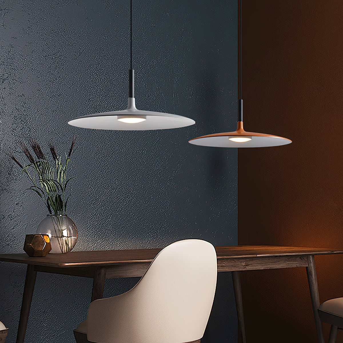 Two Clérachic pendants, one grey and one orange, hung over a wooden table in front of a dark blue wall.