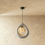 Clérachic light grey roughcast teardrop pendant with a softly lit crater-textured globe inside the ring, on a black cord.