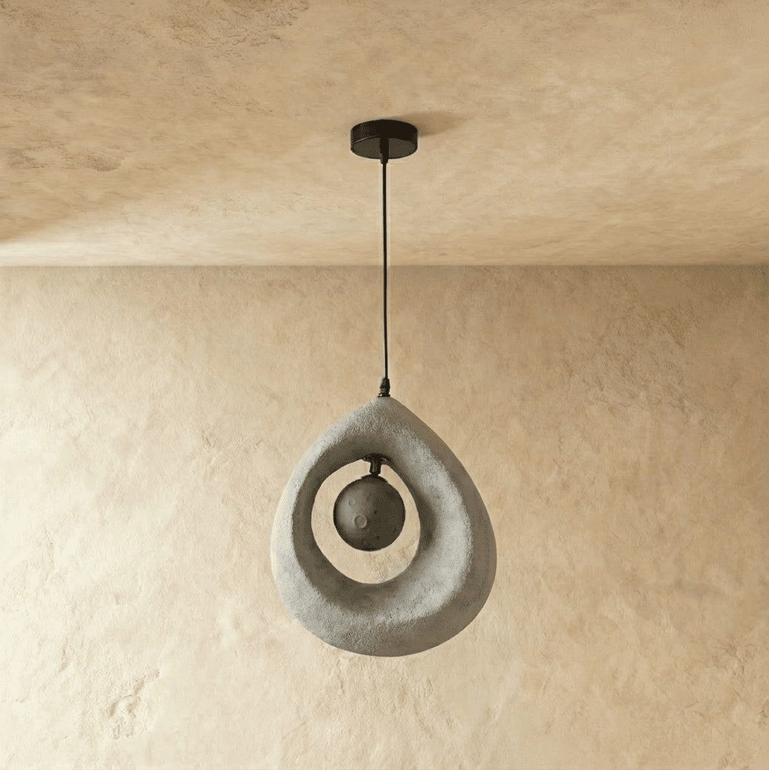 Clérachic light grey roughcast teardrop pendant with the dark crater-textured globe unlit inside its open ring.