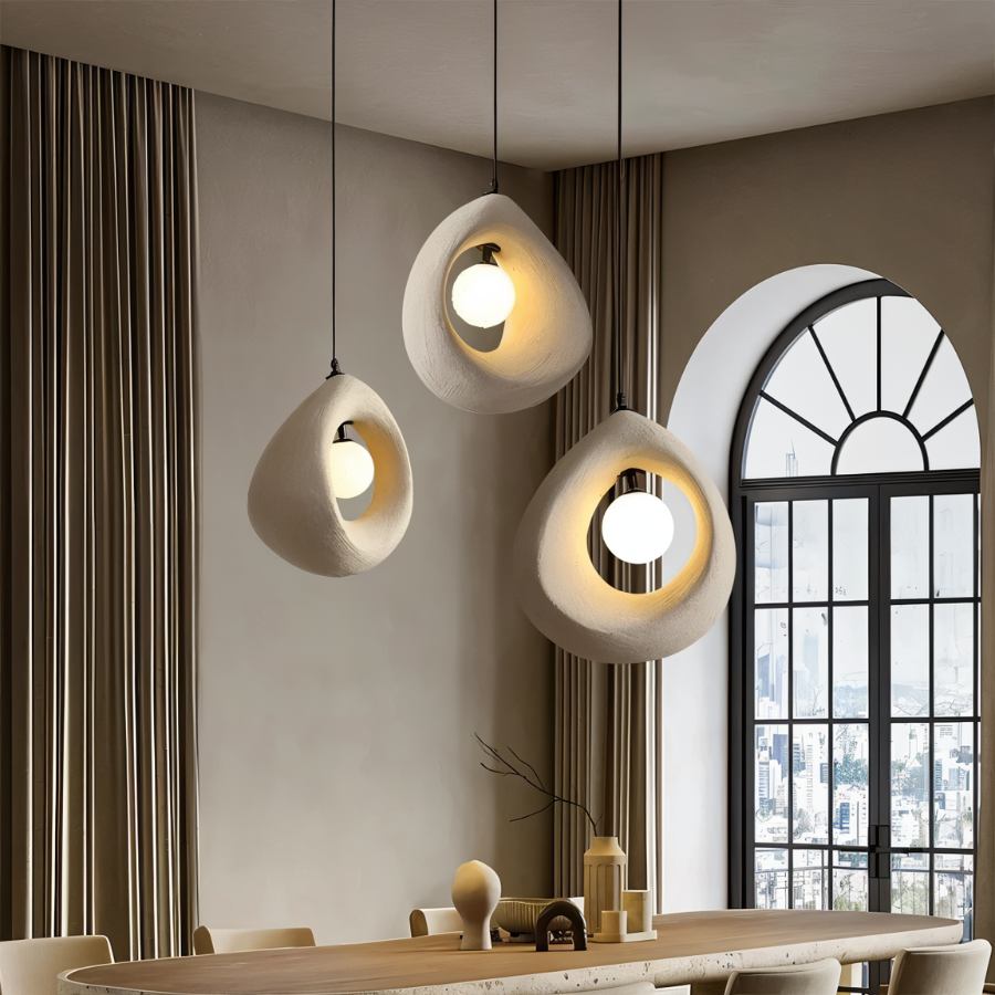 Clérachic trio of off-white textured teardrop pendants with glowing round bulbs over a long dining table by an arched window.
