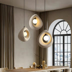 Clérachic trio of off-white textured teardrop pendants with glowing round bulbs over a long dining table by an arched window.