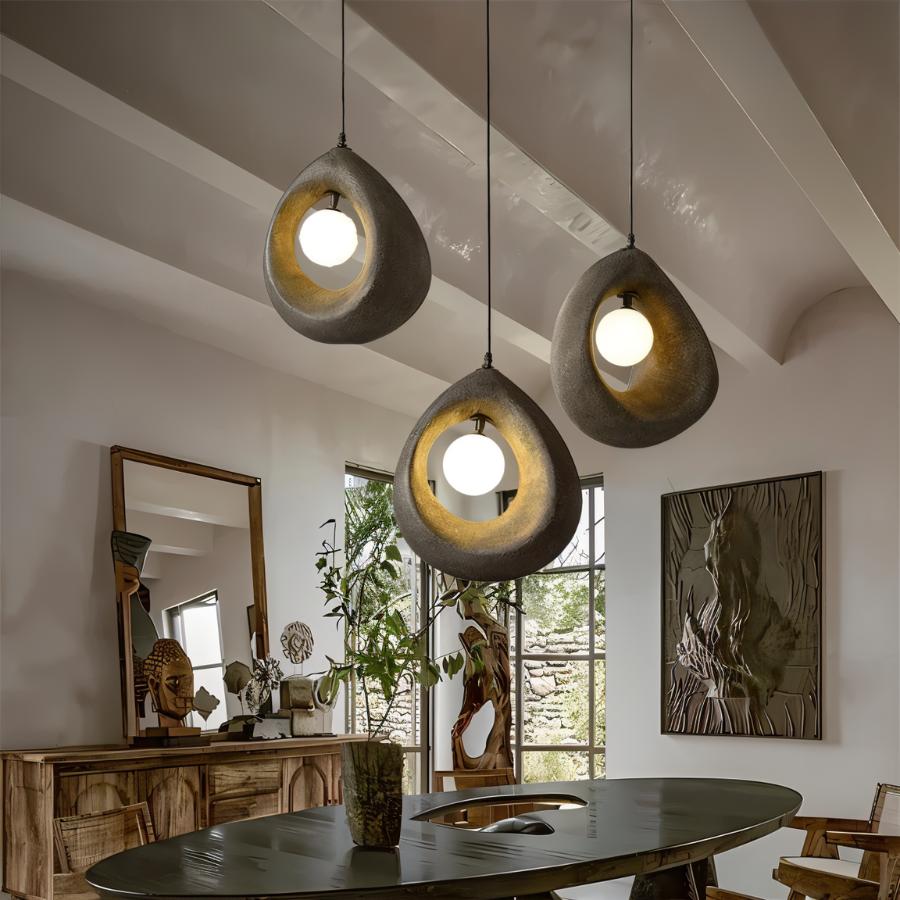 Clérachic trio of dark grey textured teardrop pendants with lit round bulbs over an oval dark dining table in a beamed room.