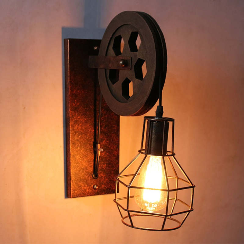 Clérachic pulley sconce lit close on a dark wall, filament glowing inside the wrought cage.