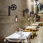 A row of Clérachic pulley sconces on a concrete wall above white-clothed restaurant tables.