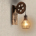 The Clérachic pulley sconce against a woven rattan wall, warm bulb inside the iron cage.
