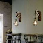 Two Clérachic pulley sconces on a sage wall above a café table and spindle-back chairs.