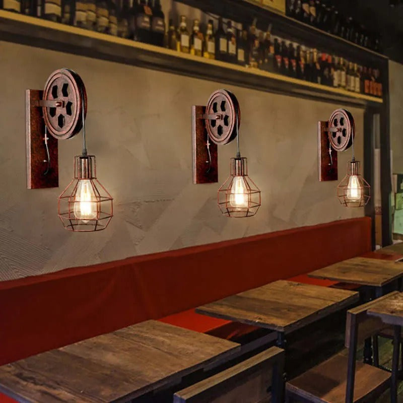 Three Clérachic pulley sconces above a bar counter lined with bottles and red banquettes.