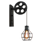 Clérachic pulley sconce in matte black, lit bulb hanging low beneath the iron wheel.