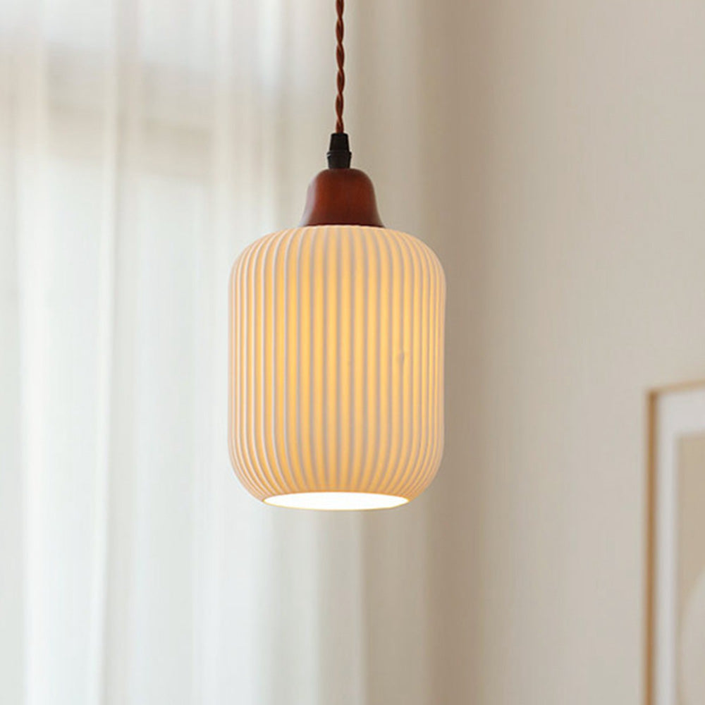A single Clérachic Ribbed Ceramic Pendant Light in the cylinder shade, lit beside a sheer curtain, its ribs catching the glow.