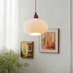 The ellipse shade of the Clérachic Ribbed Ceramic Pendant Light hanging on its twisted brown flex beside two framed paintings.