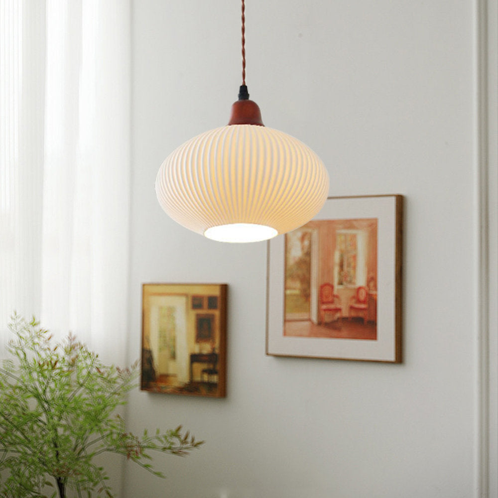 The ellipse shade of the Clérachic Ribbed Ceramic Pendant Light hanging on its twisted brown flex beside two framed paintings.