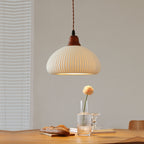 Clérachic Ribbed Ceramic Pendant Light in the dome shade, lit low over an oak dining table set with bread and a glass vase.