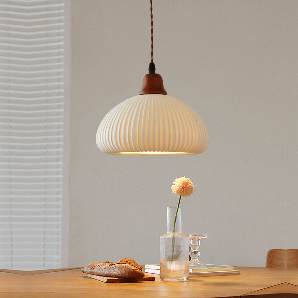 Clérachic Ribbed Ceramic Pendant Light in the dome shade, lit low over an oak dining table set with bread and a glass vase.