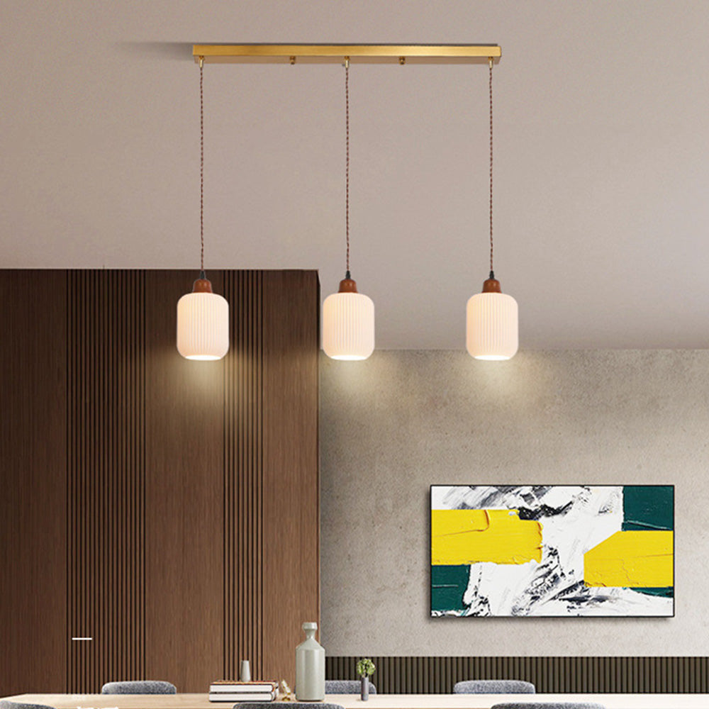 Three cylinder shades of the Clérachic Ribbed Ceramic Pendant Light on one brushed brass bar above a dining table.