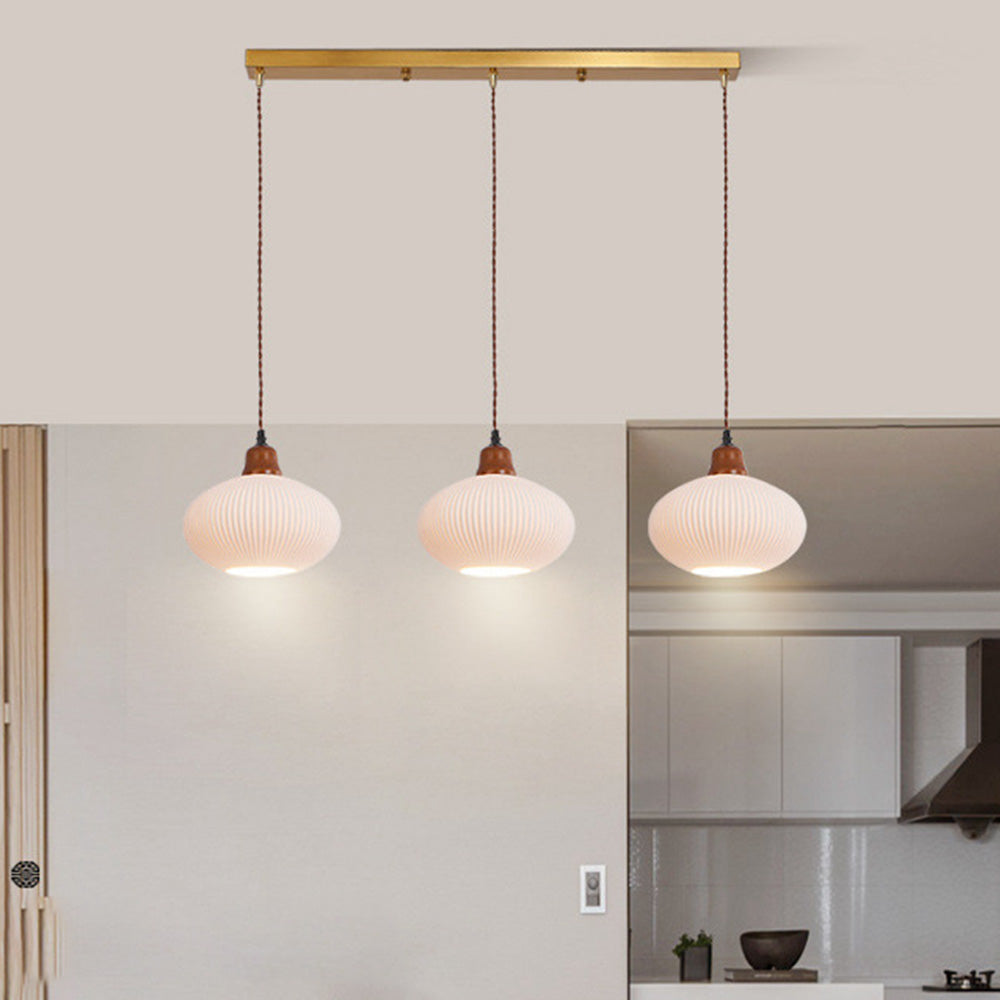 Three ellipse shades of the Clérachic Ribbed Ceramic Pendant Light lined up on a brass bar across an open kitchen.