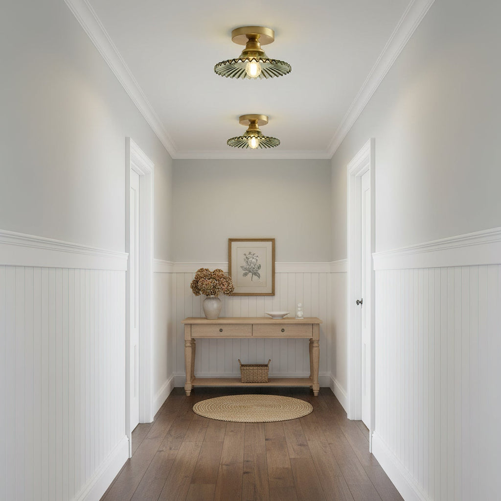 Two green ribbed glass Clérachic ceiling lights lit along a white panelled hallway, with a pale wood console at the far end.