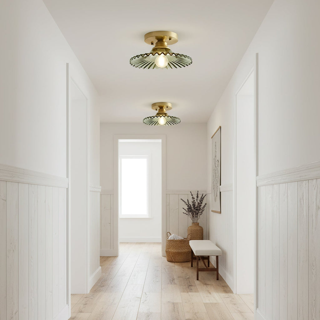Gold-finish Clérachic ceiling lights with green glass shades, glowing down a long hallway towards a bright window and a bench.