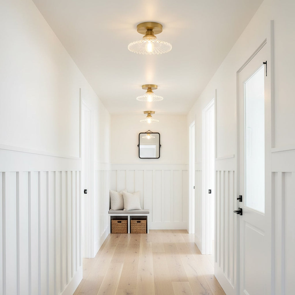 A row of clear ribbed glass Clérachic flush lights running down a white hallway, with a basket bench at the far end.