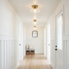 A row of clear ribbed glass Clérachic flush lights running down a white hallway, with a basket bench at the far end.