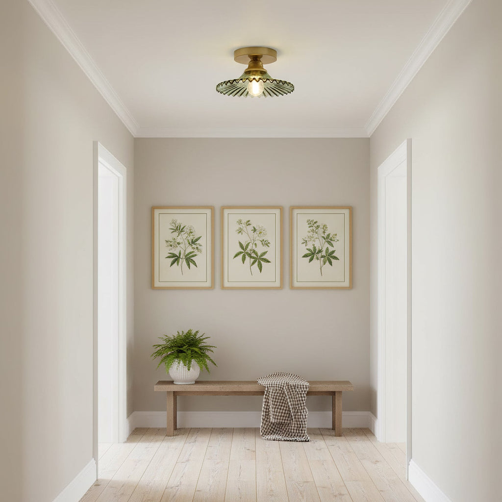 Single green glass Clérachic ceiling light in a small entrance hall, above a wooden bench and three botanical prints.