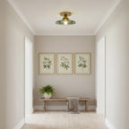 Single green glass Clérachic ceiling light in a small entrance hall, above a wooden bench and three botanical prints.