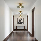 Three green glass Clérachic ceiling lights receding down a hallway with dark wood floors and a console under an abstract print.