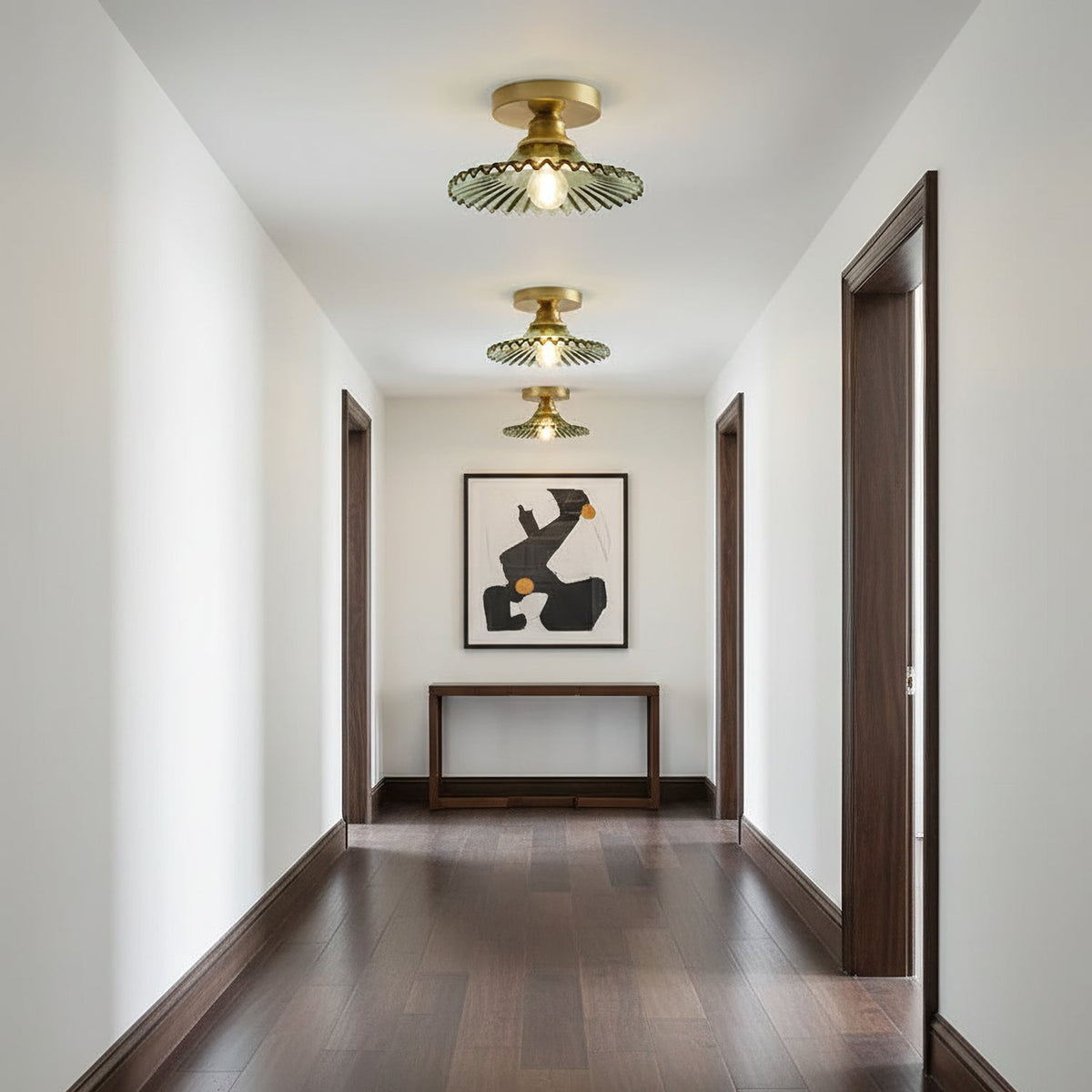 Three green glass Clérachic ceiling lights receding down a hallway with dark wood floors and a console under an abstract print.