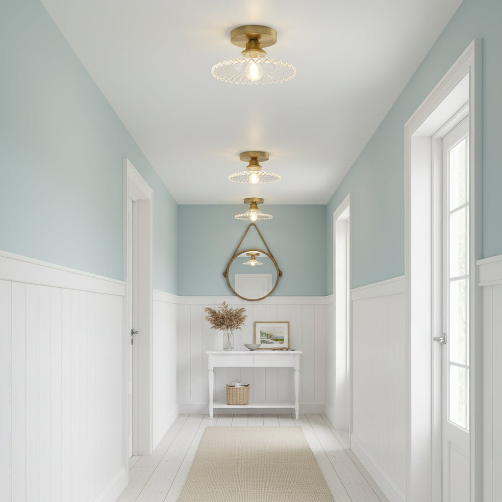 Clear ribbed glass Clérachic ceiling lights in a hallway with pale blue walls, white panelling and a round hanging mirror.