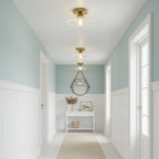 Clear ribbed glass Clérachic ceiling lights in a hallway with pale blue walls, white panelling and a round hanging mirror.