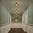 Green glass Clérachic ceiling lights lining a hallway with sage-green panelled walls and a gilt mirror at the end.