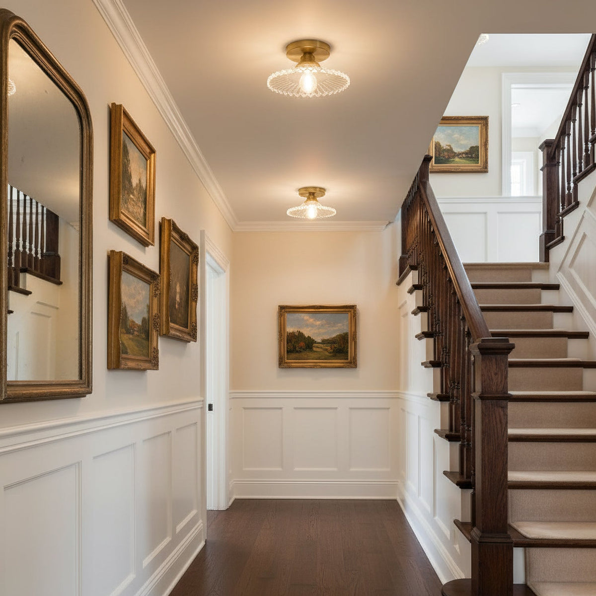Clear ribbed glass Clérachic ceiling lights above a staircase landing, with framed paintings and white panelling along the wall.