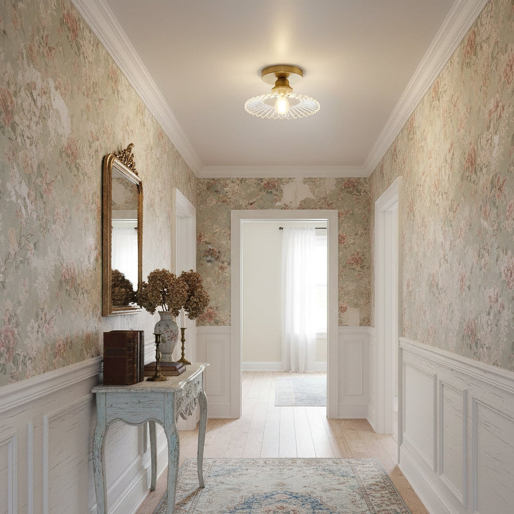 A clear glass Clérachic flush light in a hallway papered in a faded floral pattern, with a pale blue console table beneath.