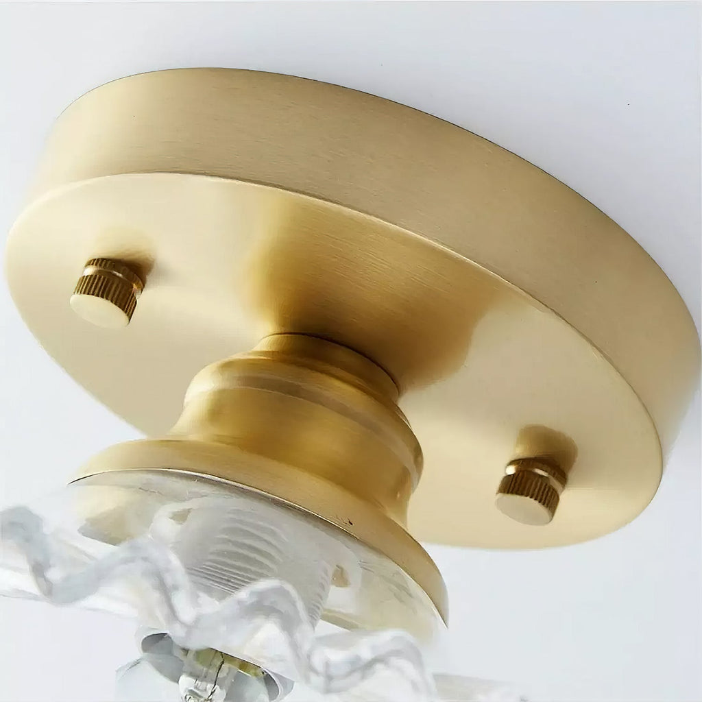Close view from below of the gold canopy and two knurled screws on this Clérachic ceiling light, with the glass shade edge below.