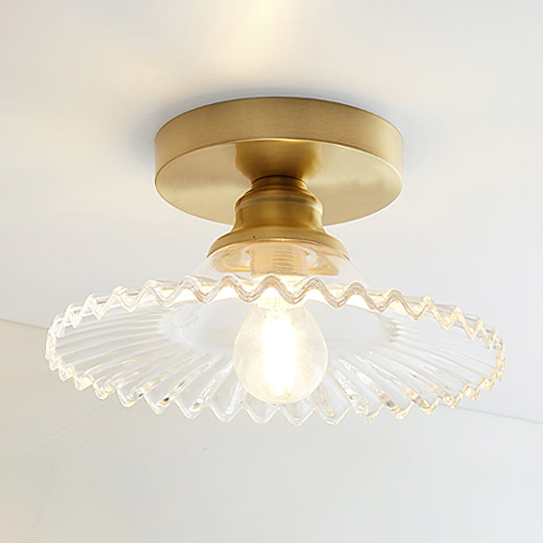 Clear ribbed glass Clérachic ceiling light, lit, with a gold canopy and a round filament bulb under a white ceiling.