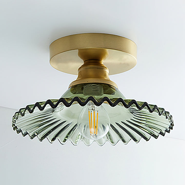 Close view of the green ribbed glass shade on this Clérachic ceiling light, with its dark wavy rim and an unlit filament bulb.