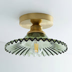 Close view of the green ribbed glass shade on this Clérachic ceiling light, with its dark wavy rim and an unlit filament bulb.