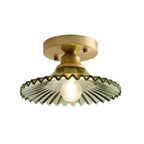 Green ribbed glass Clérachic flush light lit on a plain white backdrop, with a gold canopy and a small frosted bulb.