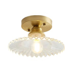 Clear ribbed glass Clérachic flush light lit on a plain white backdrop, its wavy rim spreading wide under a gold canopy.