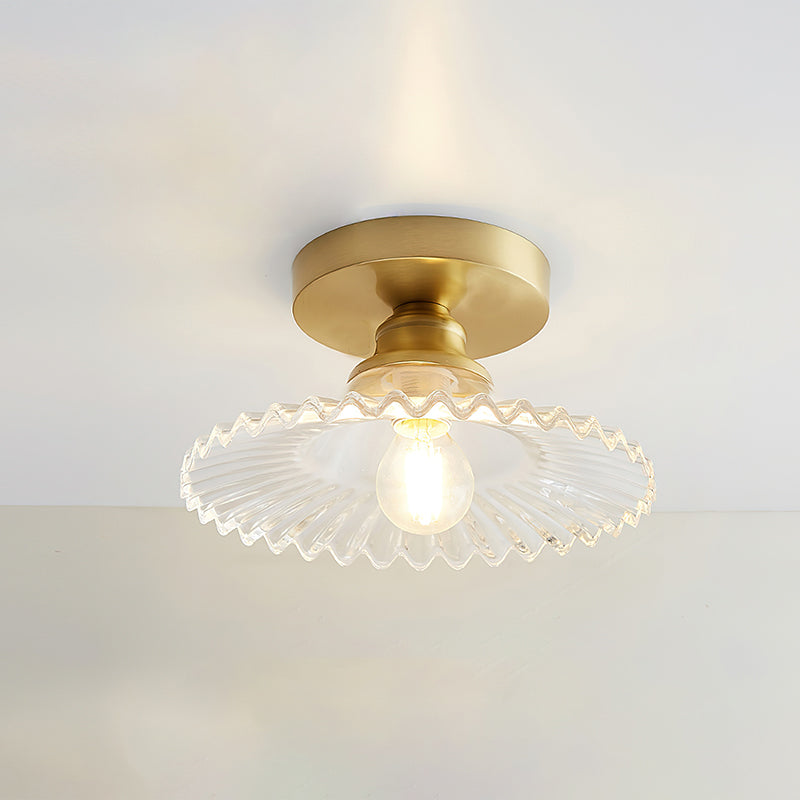 Clear glass Clérachic ceiling light with a warm lit bulb and a gold canopy, photographed against a soft grey ceiling.