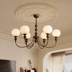 This Clérachic chandelier hangs beneath a moulded ceiling rose, its six ribbed white globes lit against a cream wall and sheer curtains.
