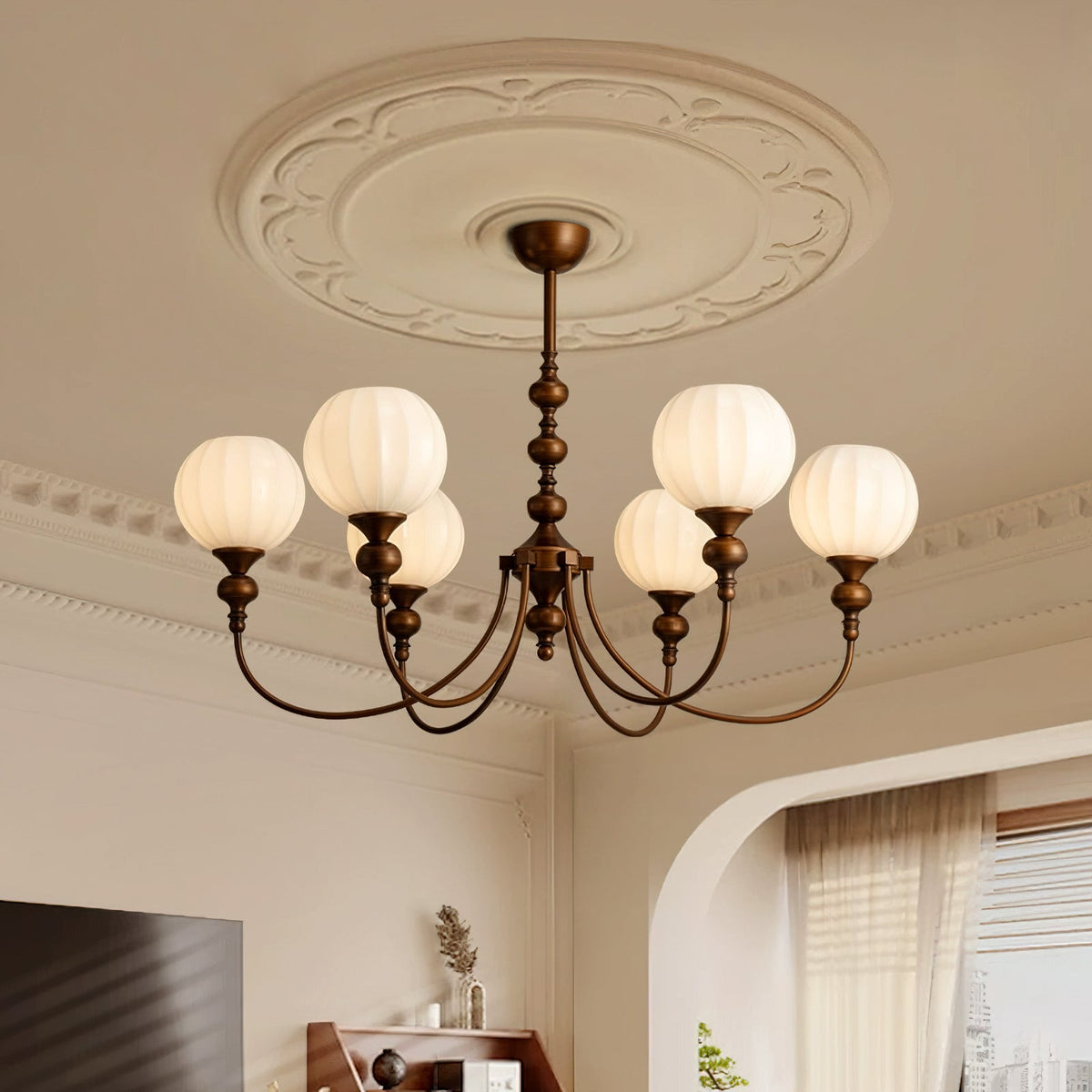 This Clérachic chandelier hangs beneath a moulded ceiling rose, its six ribbed white globes lit against a cream wall and sheer curtains.