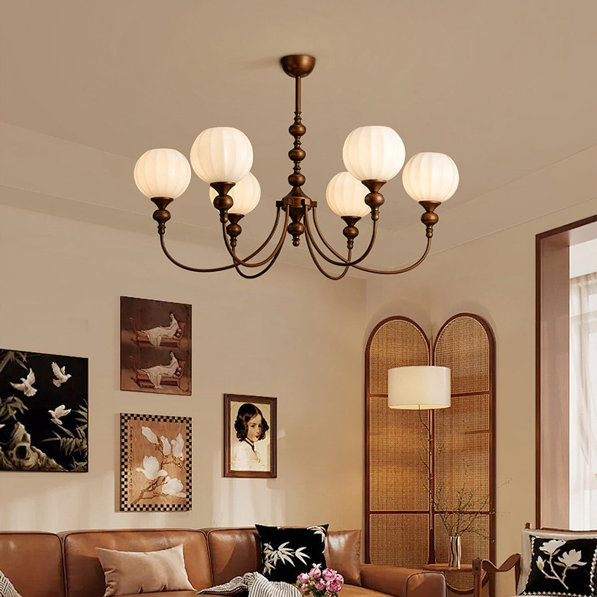 A Clérachic chandelier with ribbed glass globes and bronze arms, hung in a living room with a tan leather sofa and a tall arched screen.