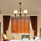 Three-light Clérachic chandelier with ribbed white globes, hanging in front of a window with orange blinds and brown curtains.