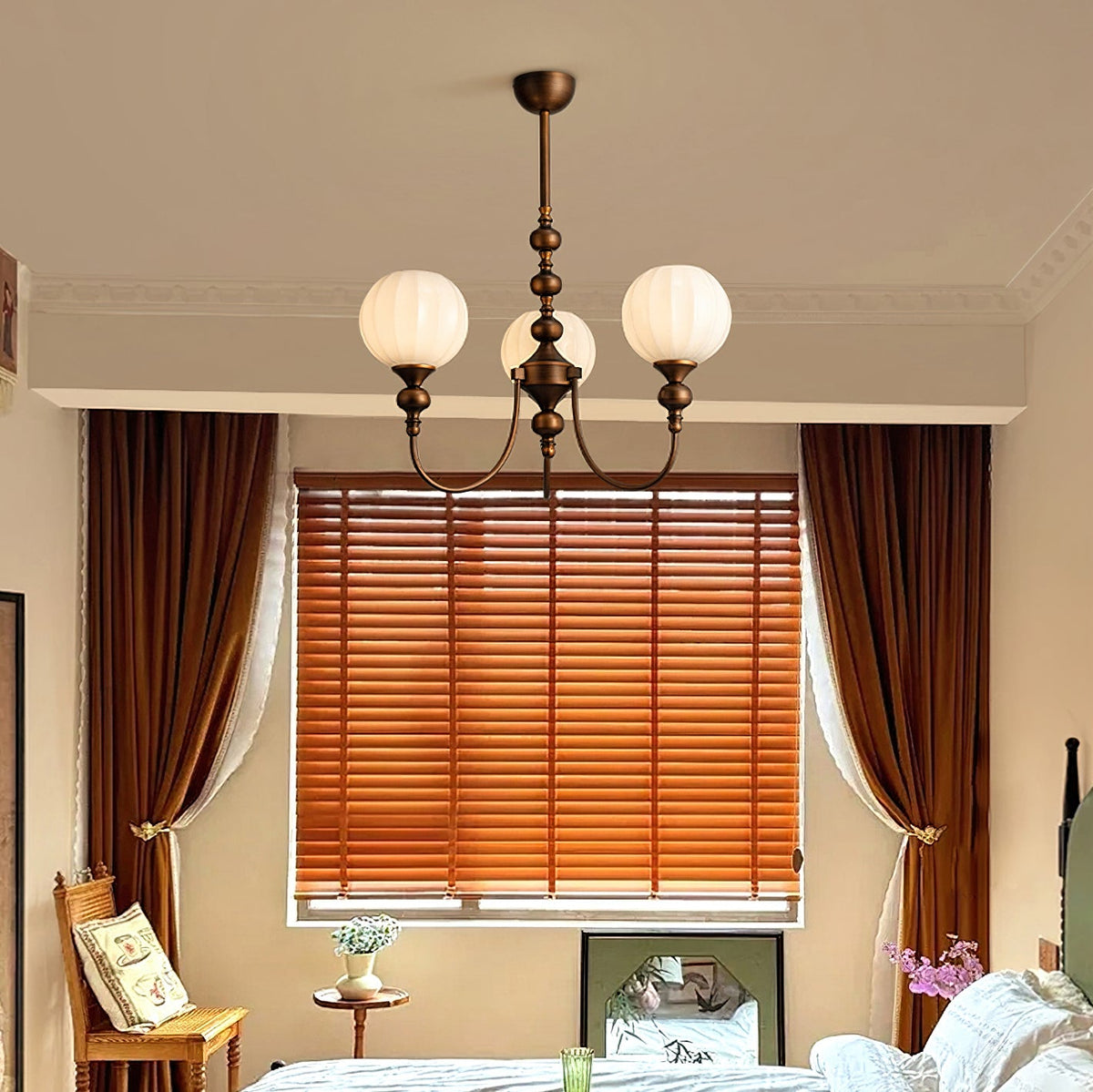 Three-light Clérachic chandelier with ribbed white globes, hanging in front of a window with orange blinds and brown curtains.
