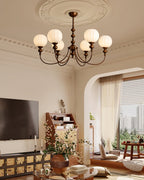 Wide view of a Clérachic chandelier with six globes in a room with an arched doorway, a wall-mounted television and a carved sideboard.
