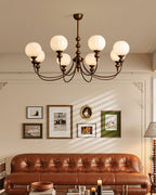 An eight-light Clérachic chandelier with ribbed globes and bronze arms, hung above a buttoned tan leather sofa and a framed picture wall.