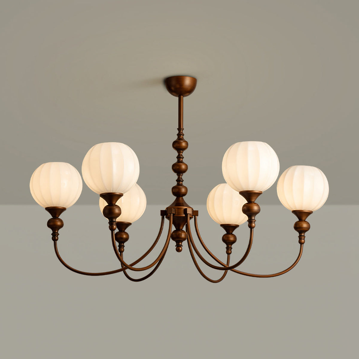 A six-light Clérachic chandelier with ribbed glass globes and arched bronze arms, lit against a grey wall.