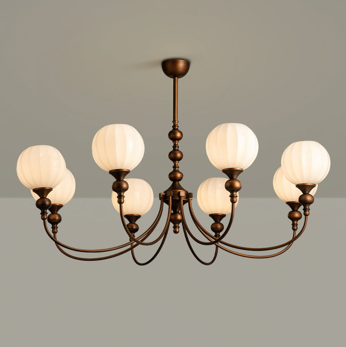 This Clérachic chandelier lit on a grey backdrop, six ribbed globes glowing warm white above the curved bronze arms.